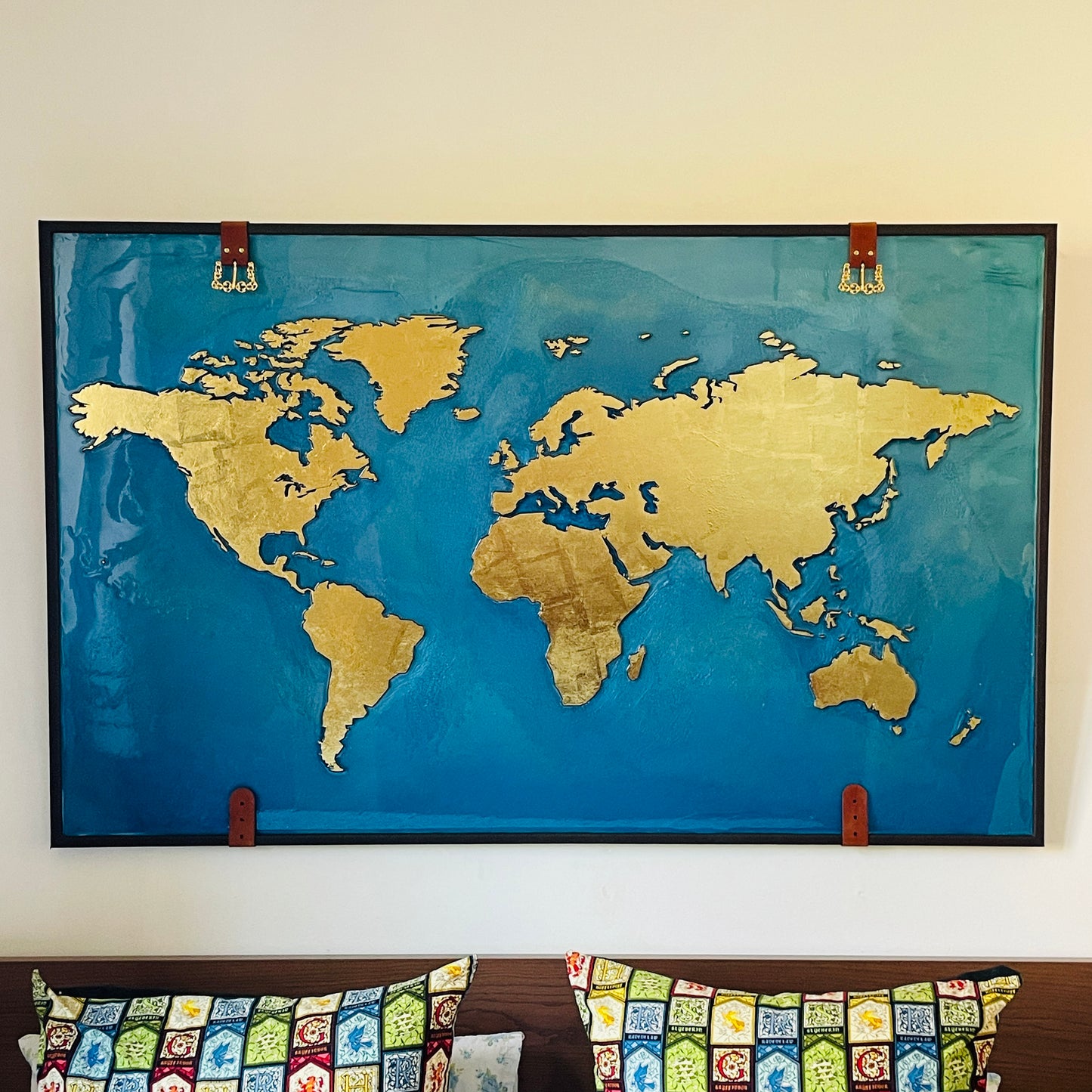 Resin world map and wooden continents covered with gold leaf in a wooden frame covered in leather and straps with golden buckles