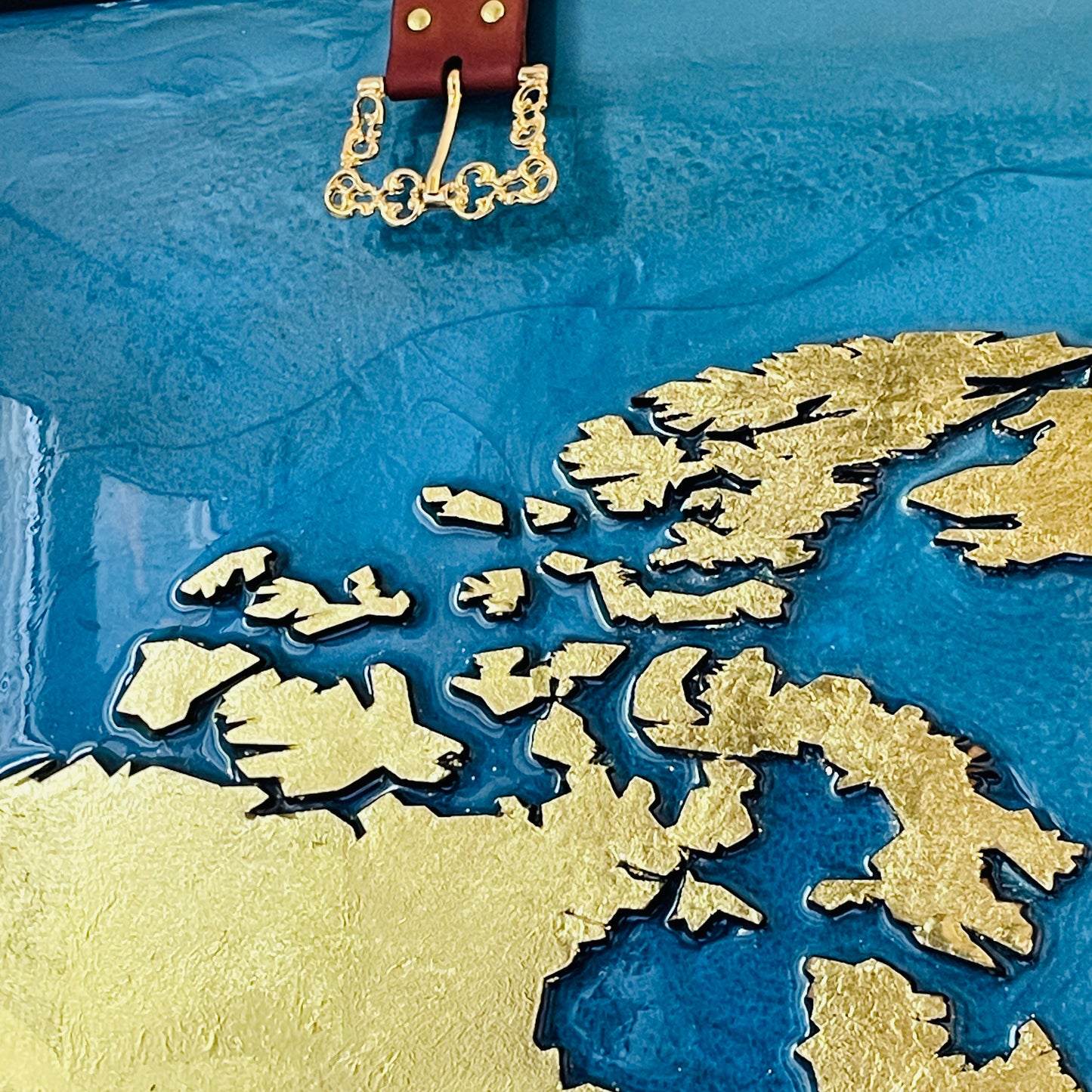 Resin world map and wooden continents covered with gold leaf in a wooden frame covered in leather and straps with golden buckles